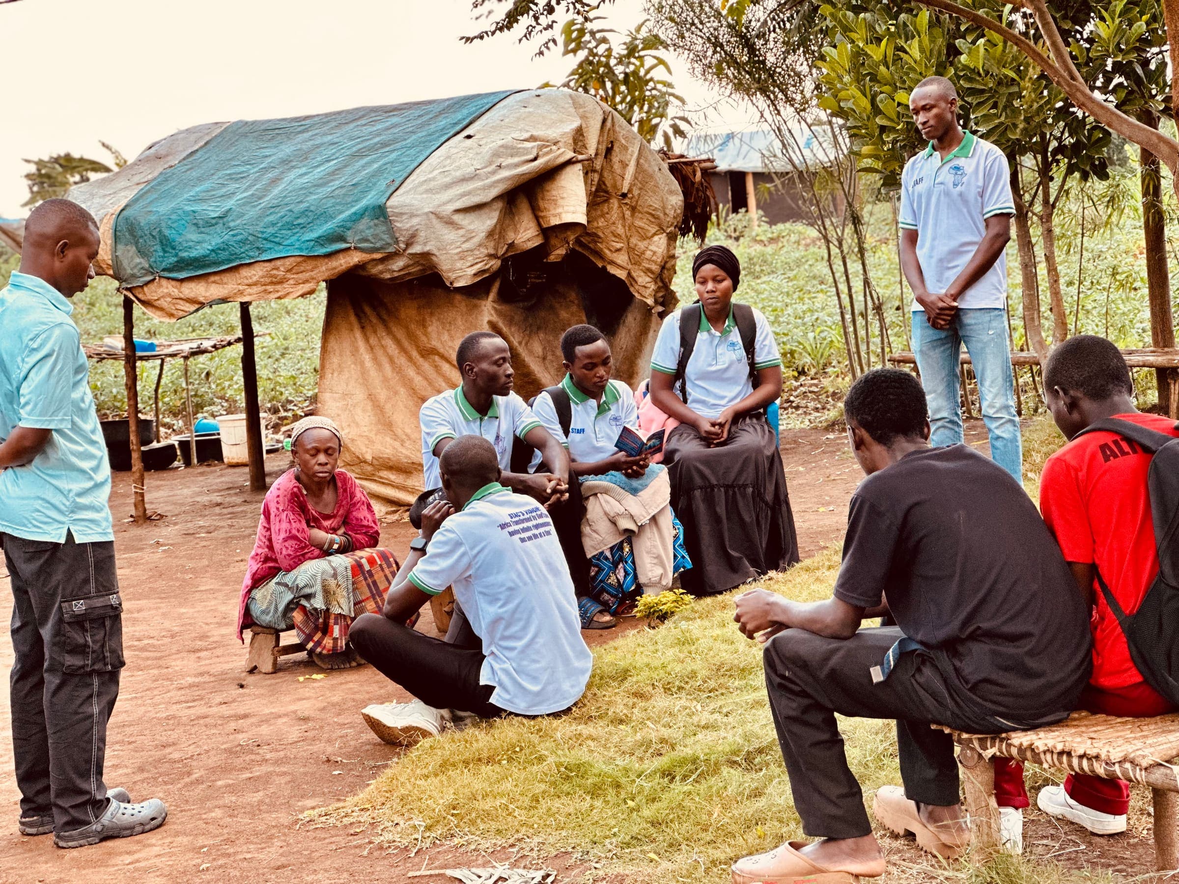 STAC team members sitting with a family outside their shelter in Kyangwali Refugee Settlement, sharing the gospel